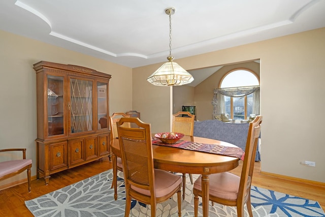 dining space featuring a tray ceiling, a notable chandelier, and wood finished floors