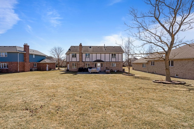 rear view of property featuring brick siding, a patio area, a lawn, and a chimney