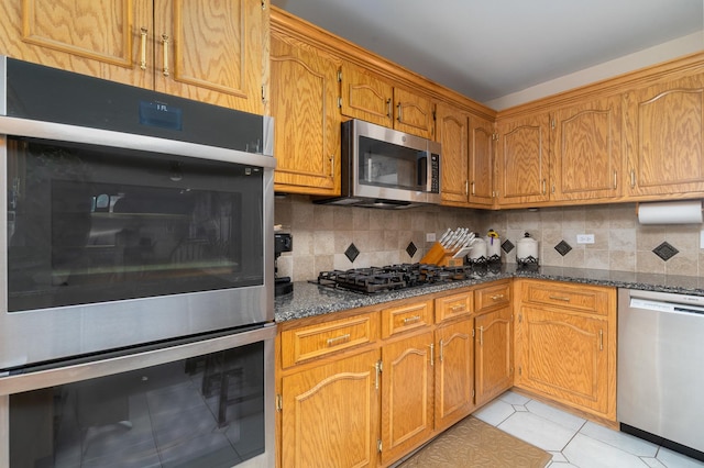 kitchen featuring dark stone countertops, brown cabinets, tasteful backsplash, and appliances with stainless steel finishes