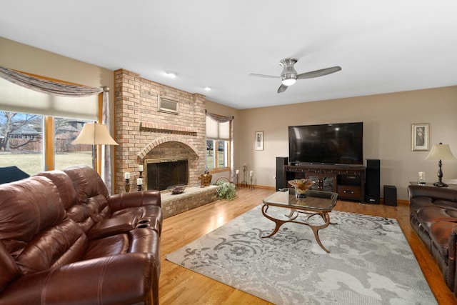 living room with a brick fireplace, baseboards, ceiling fan, and wood finished floors