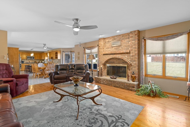 living room with light wood finished floors, visible vents, a brick fireplace, baseboards, and ceiling fan