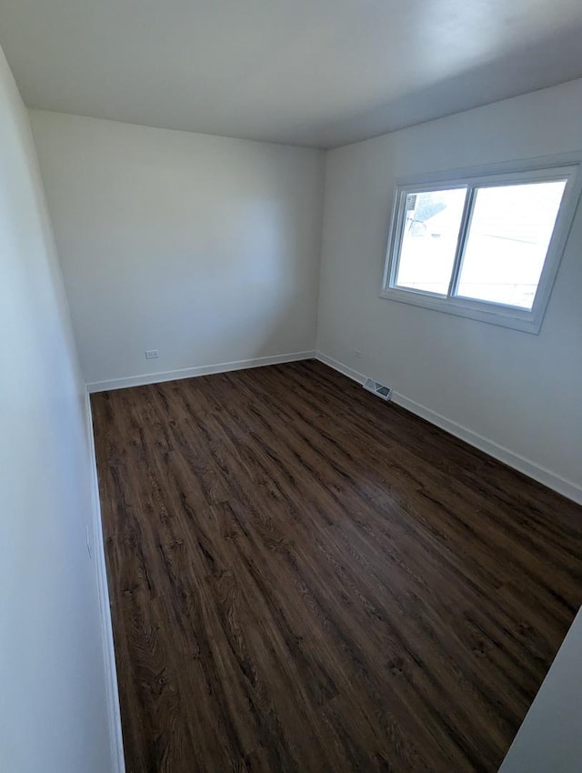 spare room featuring dark wood-style floors, visible vents, and baseboards