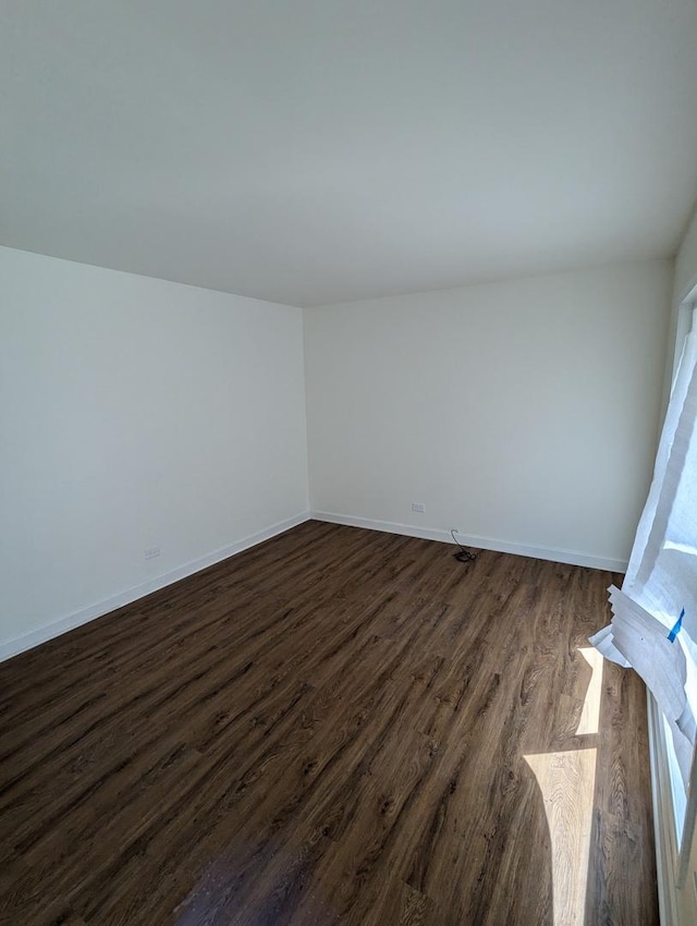 spare room with lofted ceiling, dark wood-type flooring, and baseboards