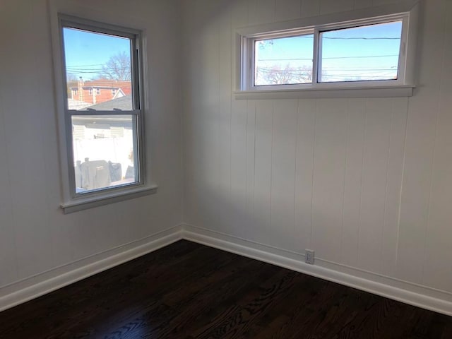 spare room with dark wood-type flooring, plenty of natural light, and baseboards