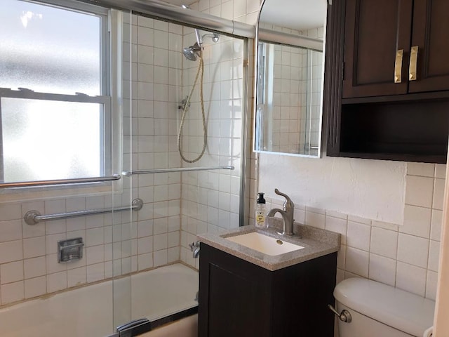 full bath with bath / shower combo with glass door, vanity, toilet, and tile walls