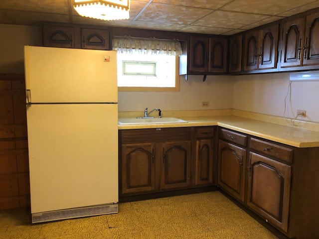 kitchen with dark brown cabinetry, freestanding refrigerator, light countertops, a paneled ceiling, and a sink