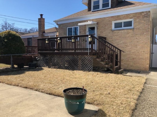 view of front of property with a wooden deck, fence, a front lawn, and brick siding