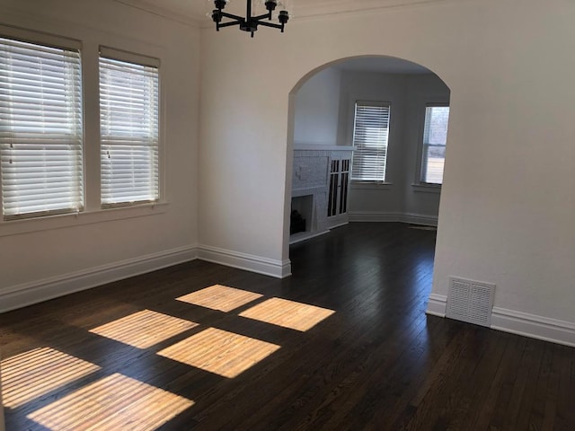 unfurnished living room featuring arched walkways, wood-type flooring, visible vents, and a fireplace with raised hearth