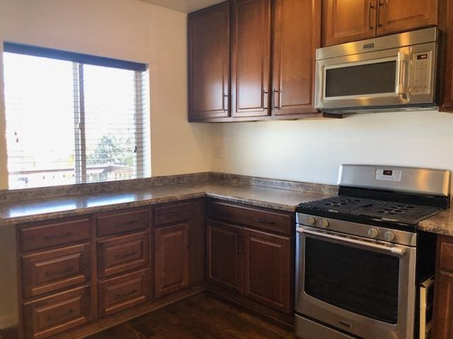 kitchen with dark countertops, a peninsula, stainless steel appliances, and dark wood finished floors