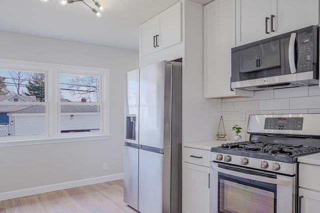 kitchen with appliances with stainless steel finishes, backsplash, white cabinetry, and light wood-style floors