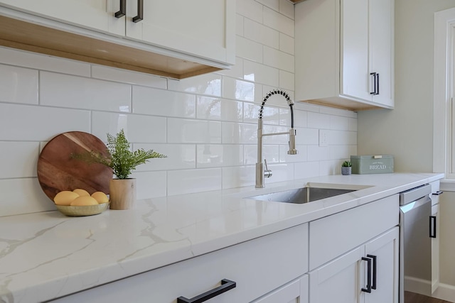 kitchen featuring light stone counters, a sink, white cabinetry, backsplash, and dishwasher