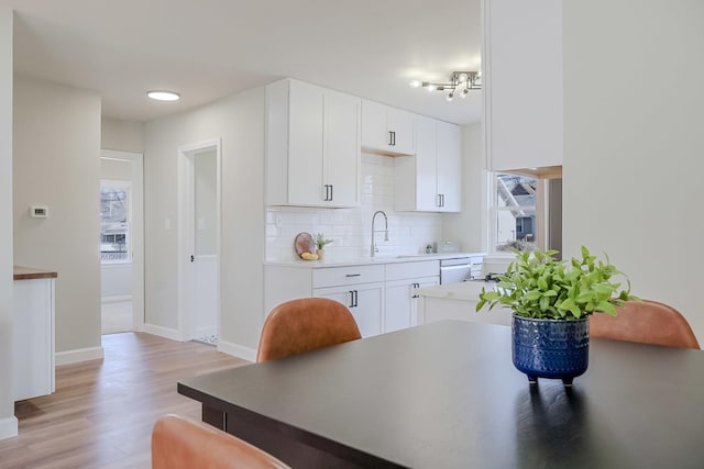 kitchen with light countertops, decorative backsplash, light wood-style floors, white cabinetry, and a sink