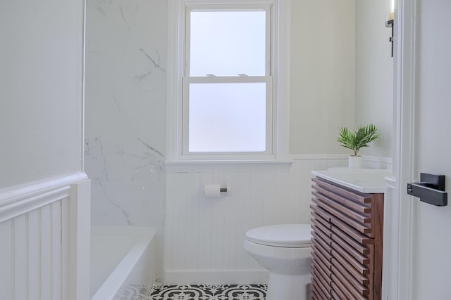 full bathroom with toilet, a wainscoted wall, a tub to relax in, and vanity