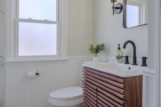 half bath with a wainscoted wall, vanity, and toilet