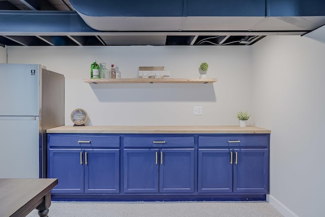 kitchen with blue cabinetry, open shelves, light countertops, and freestanding refrigerator