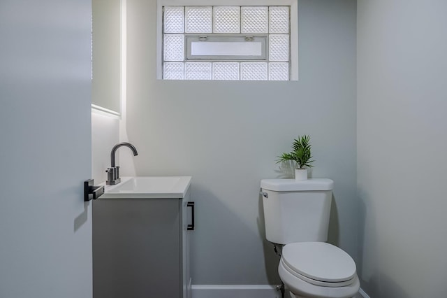 half bathroom with baseboards, vanity, and toilet