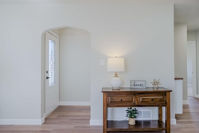 entryway featuring arched walkways, light wood-style flooring, and baseboards