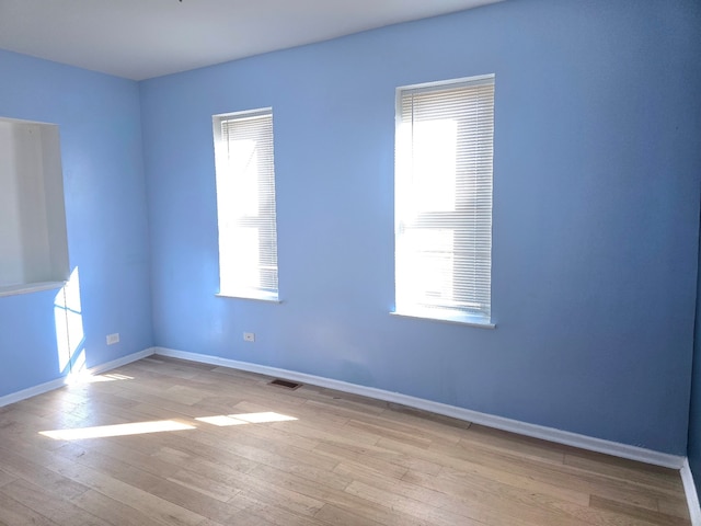 empty room featuring a healthy amount of sunlight, baseboards, visible vents, and wood finished floors