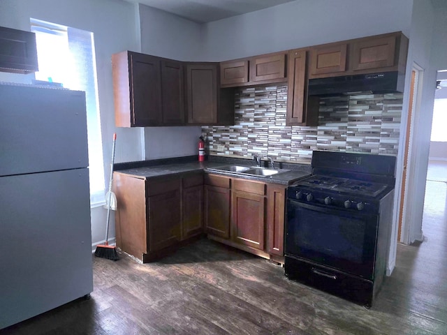 kitchen featuring black range with gas cooktop, a sink, freestanding refrigerator, dark countertops, and dark wood finished floors