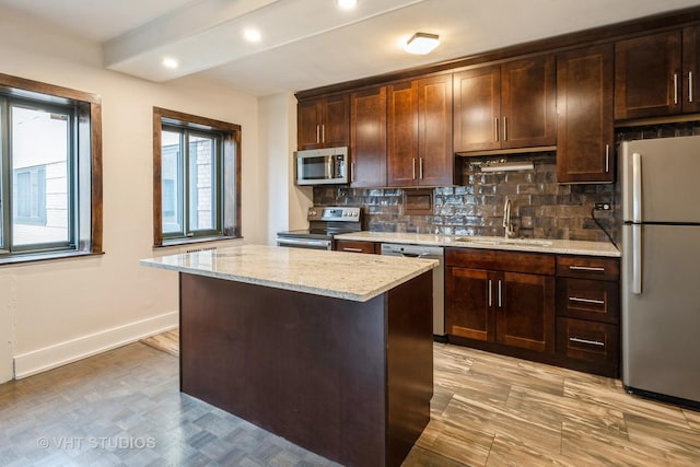 kitchen with tasteful backsplash, a kitchen island, appliances with stainless steel finishes, a sink, and baseboards