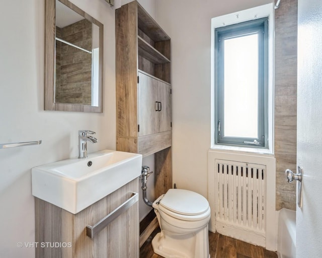 bathroom with toilet, radiator heating unit, vanity, and wood finished floors