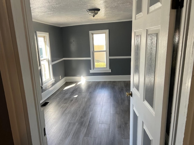 empty room featuring dark wood-style floors, visible vents, a textured ceiling, and baseboards