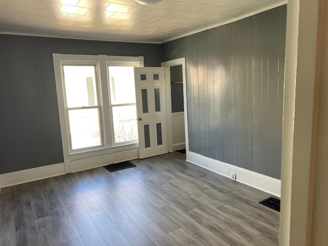 empty room featuring visible vents, baseboards, wood finished floors, and ornamental molding