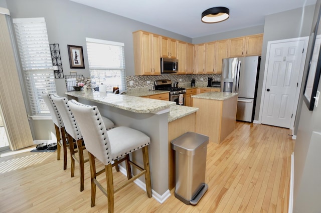 kitchen featuring stainless steel appliances, a peninsula, light brown cabinets, and decorative backsplash