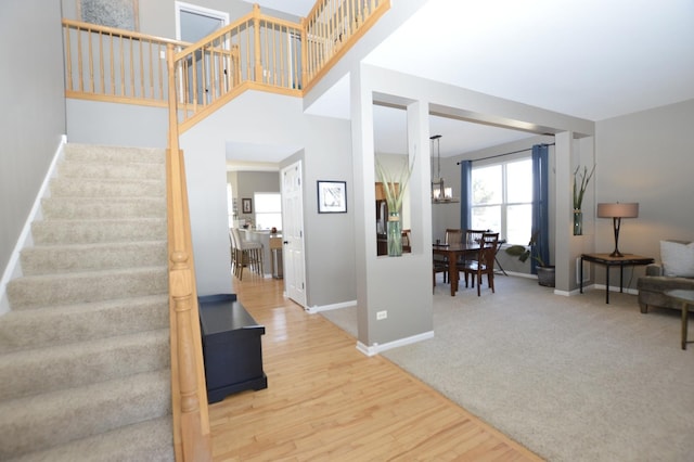 stairs featuring a chandelier, carpet floors, a high ceiling, wood finished floors, and baseboards