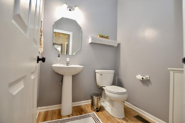 half bathroom with toilet, baseboards, visible vents, and wood finished floors