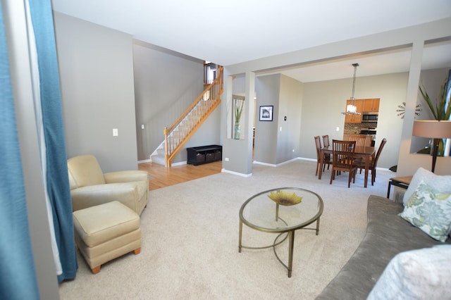 living area with stairs, light carpet, and baseboards