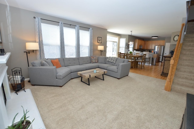 living area with light colored carpet, baseboards, and stairs