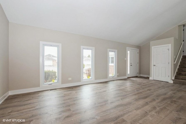 unfurnished living room with lofted ceiling, wood finished floors, visible vents, baseboards, and stairway