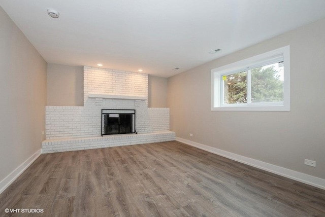 unfurnished living room with a brick fireplace, visible vents, baseboards, and wood finished floors