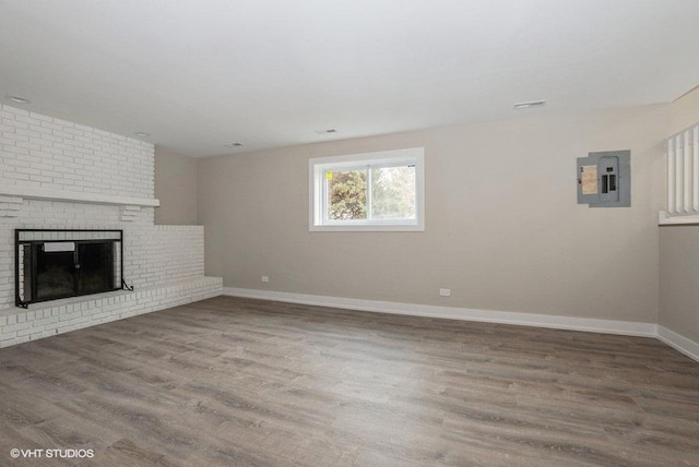 unfurnished living room featuring a brick fireplace, electric panel, baseboards, and wood finished floors