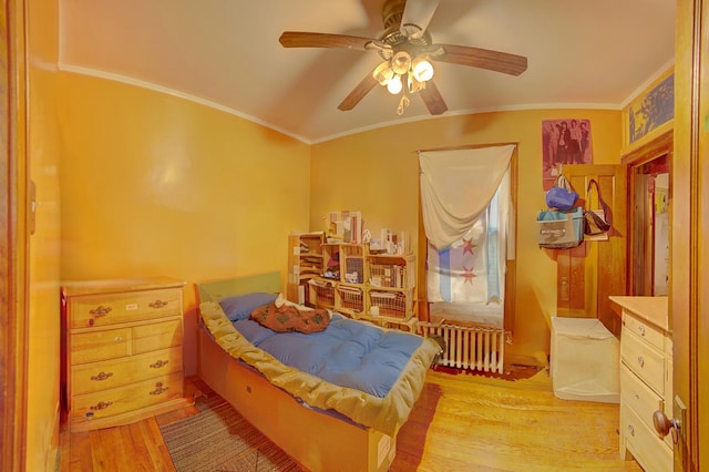 bedroom with radiator heating unit, light wood finished floors, ornamental molding, and a ceiling fan
