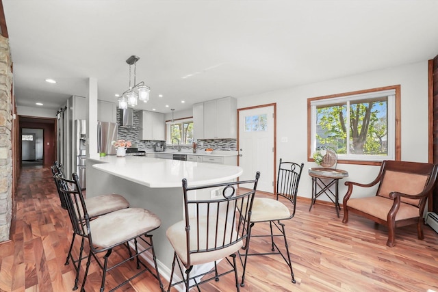 kitchen featuring a breakfast bar area, light countertops, tasteful backsplash, light wood-type flooring, and decorative light fixtures
