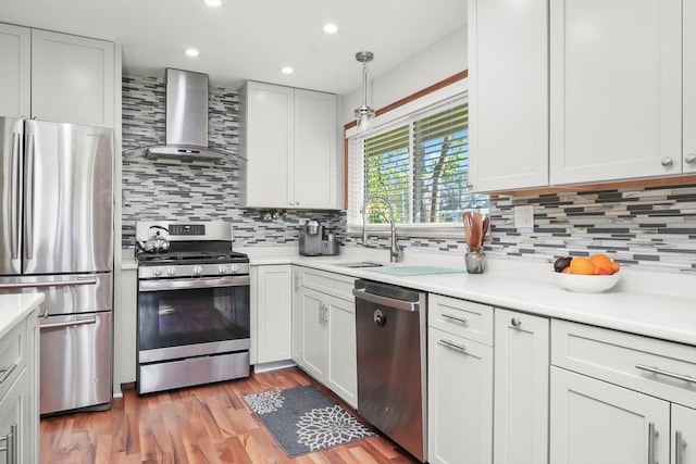 kitchen with appliances with stainless steel finishes, wall chimney range hood, tasteful backsplash, light countertops, and recessed lighting