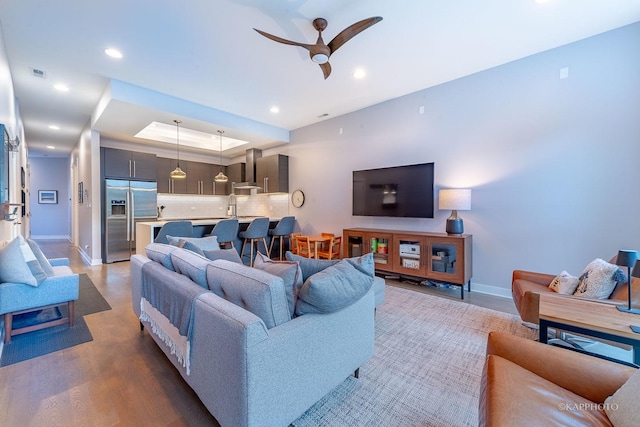 living room with ceiling fan, recessed lighting, visible vents, light wood finished floors, and a raised ceiling