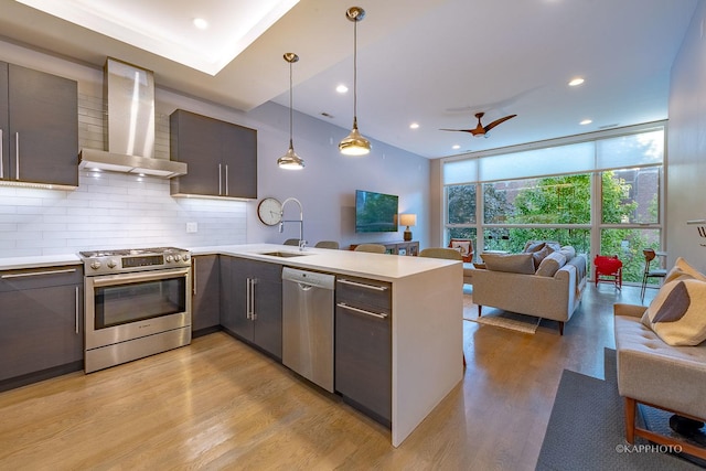 kitchen with wall chimney exhaust hood, appliances with stainless steel finishes, open floor plan, a wall of windows, and a sink