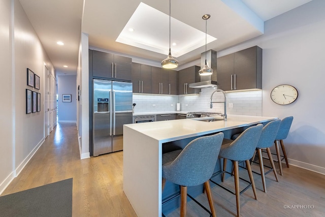 kitchen with a peninsula, a sink, backsplash, a tray ceiling, and stainless steel fridge