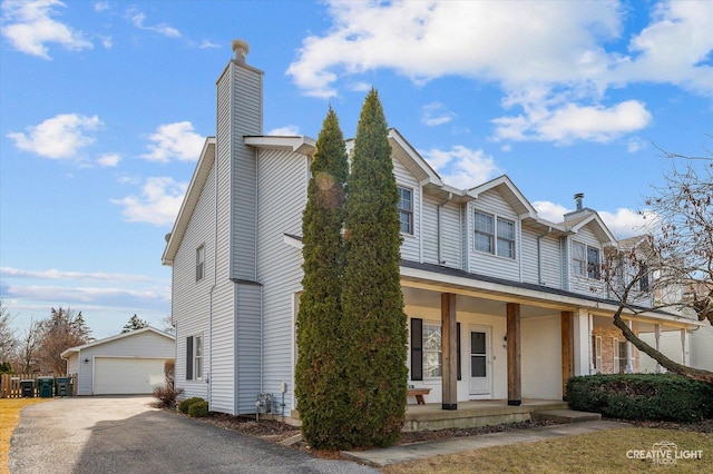 view of property featuring an outbuilding, covered porch, a detached garage, and a chimney