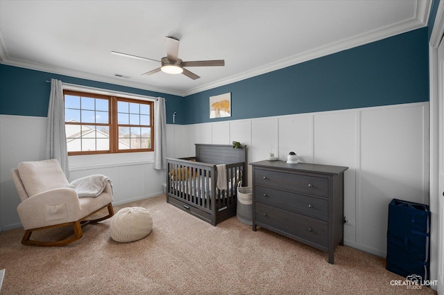 bedroom featuring visible vents, light carpet, a wainscoted wall, a nursery area, and crown molding