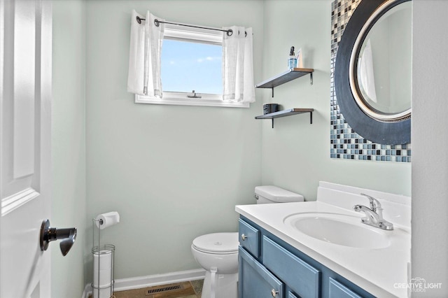 half bath featuring visible vents, baseboards, toilet, and vanity