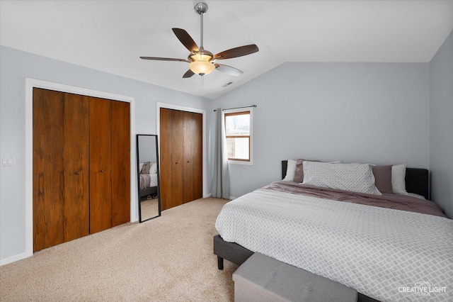 bedroom with vaulted ceiling, light colored carpet, two closets, and ceiling fan