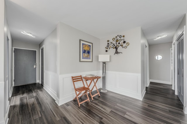 corridor featuring a wainscoted wall and dark wood-style flooring