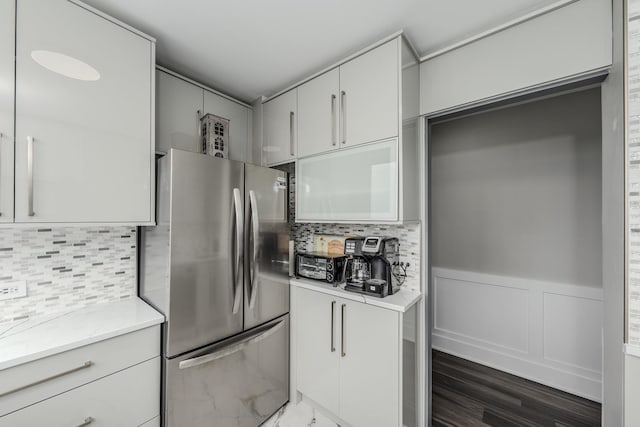 kitchen with tasteful backsplash, a wainscoted wall, white cabinetry, and freestanding refrigerator