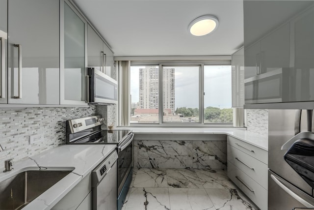 kitchen with light stone countertops, decorative backsplash, appliances with stainless steel finishes, marble finish floor, and a sink