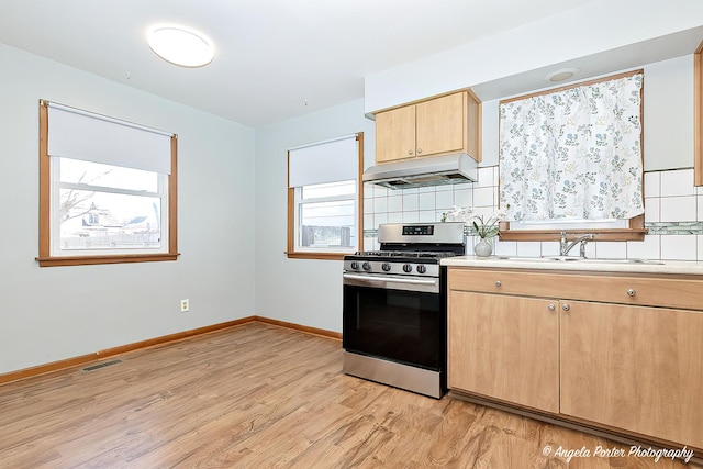 kitchen featuring visible vents, light wood-style flooring, stainless steel gas range, under cabinet range hood, and light brown cabinets