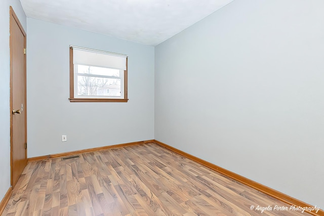 spare room with light wood finished floors, visible vents, and baseboards